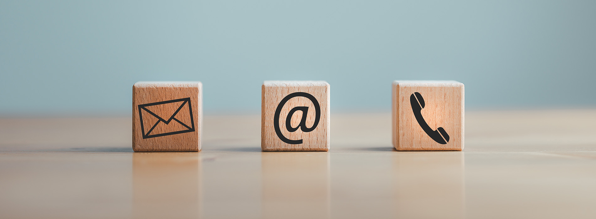 The image shows four wooden blocks with symbols representing communication methods an envelope for mail, a phone for voice calls, a computer icon for digital communication, and a smartphone symbol for mobile devices, arranged on a flat surface against a blue background.